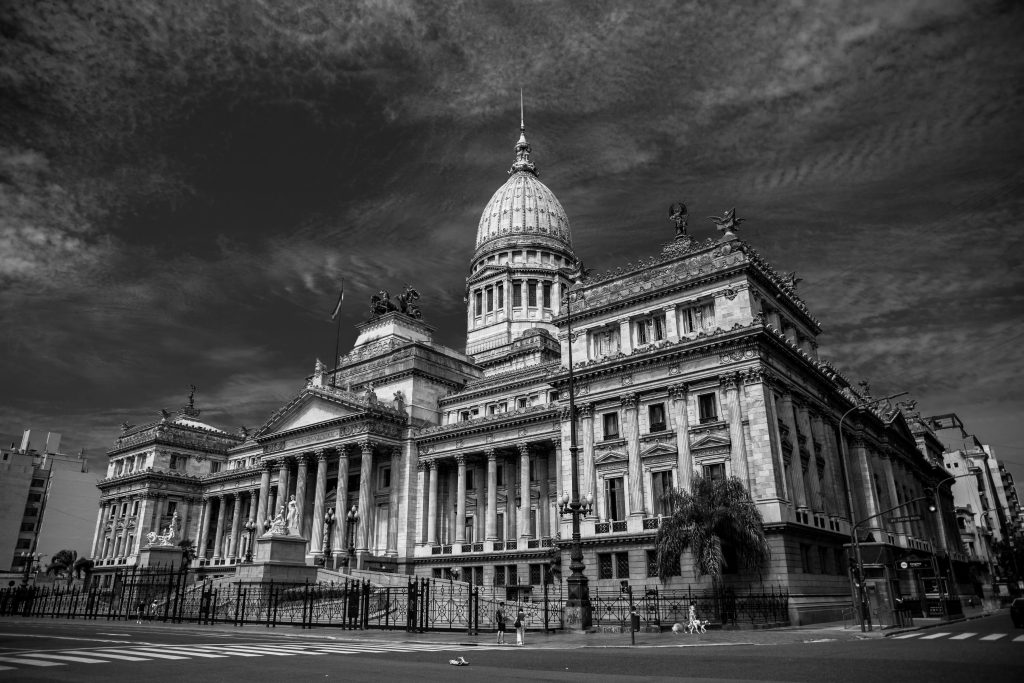 Monochrome image of a majestic capitol building with a dome and statues.